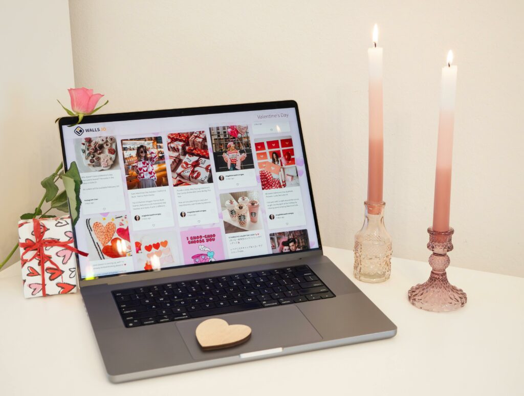 A cozy Valentine's Day-themed laptop workspace with candles, a gift, and a rose.